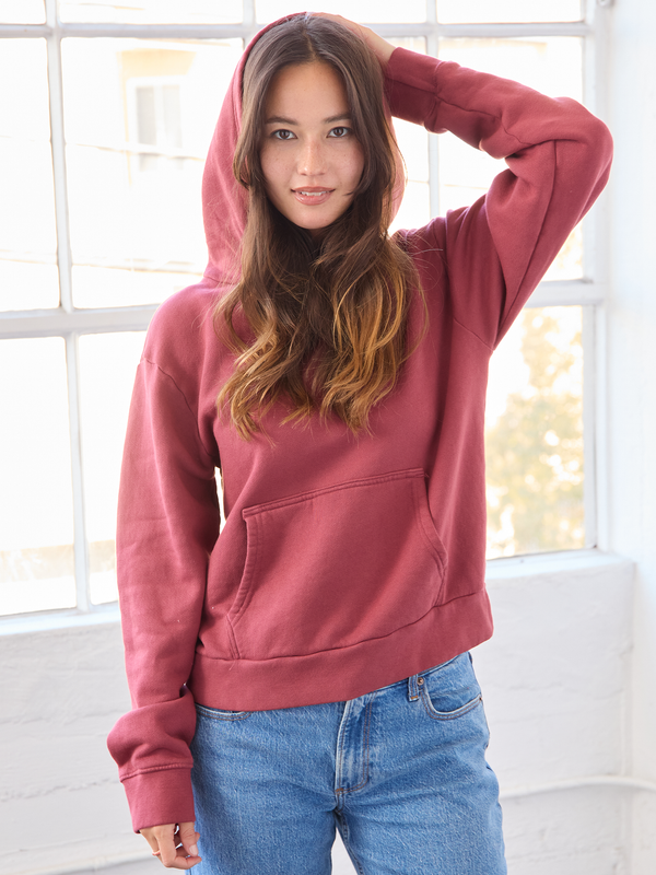 Person wearing a red hoodie and blue jeans indoors with a window in the background