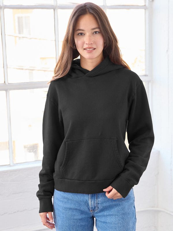 Person wearing a black hoodie and blue jeans indoors with a window in the background
