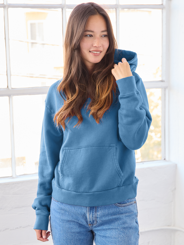 Woman wearing a blue hoodie in a bright room with large windows