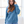 Woman wearing a blue hoodie in a bright room with large windows.
