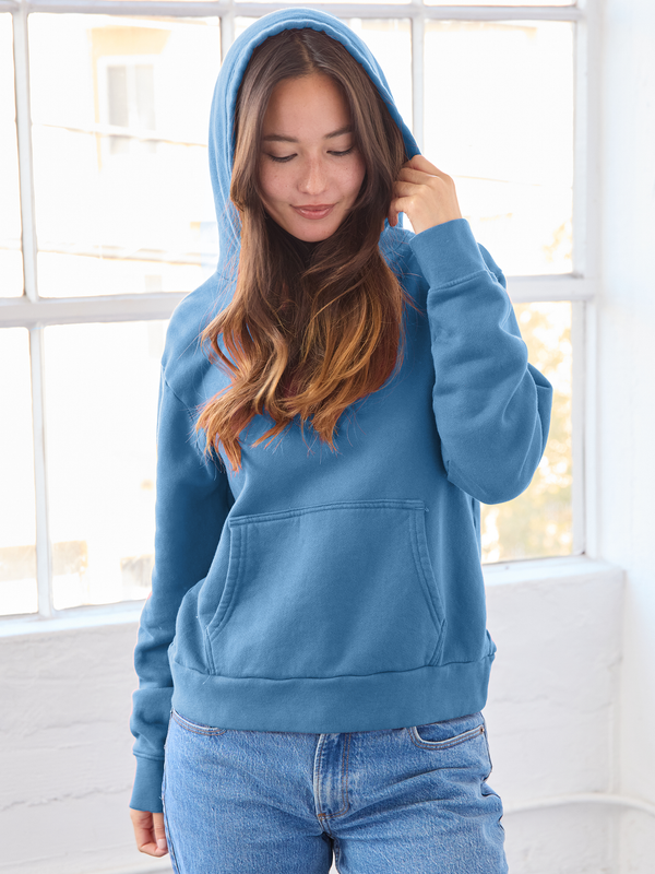 Woman wearing a blue hoodie in a bright room with large windows.