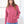 Person wearing a pink hoodie and blue jeans indoors with a window background
