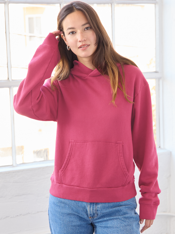 Woman wearing a pink hoodie in a bright room with large windows.