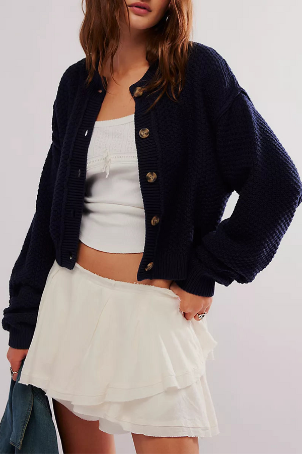 Woman wearing a navy cardigan over a white top and skirt on a plain background