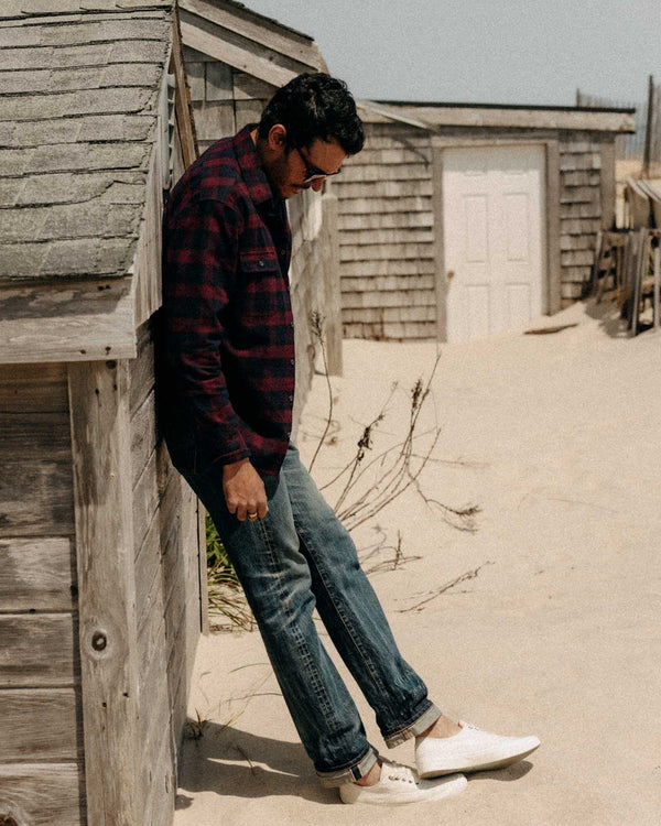 Man leaning against a wooden structure on a sandy beach.