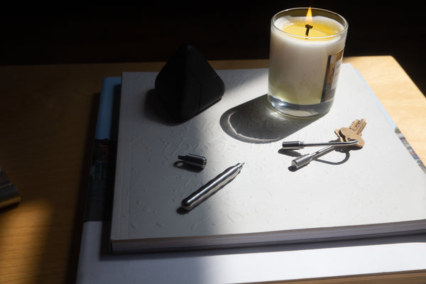 Candle in a glass holder on a table with a pen, keys, and a notebook.